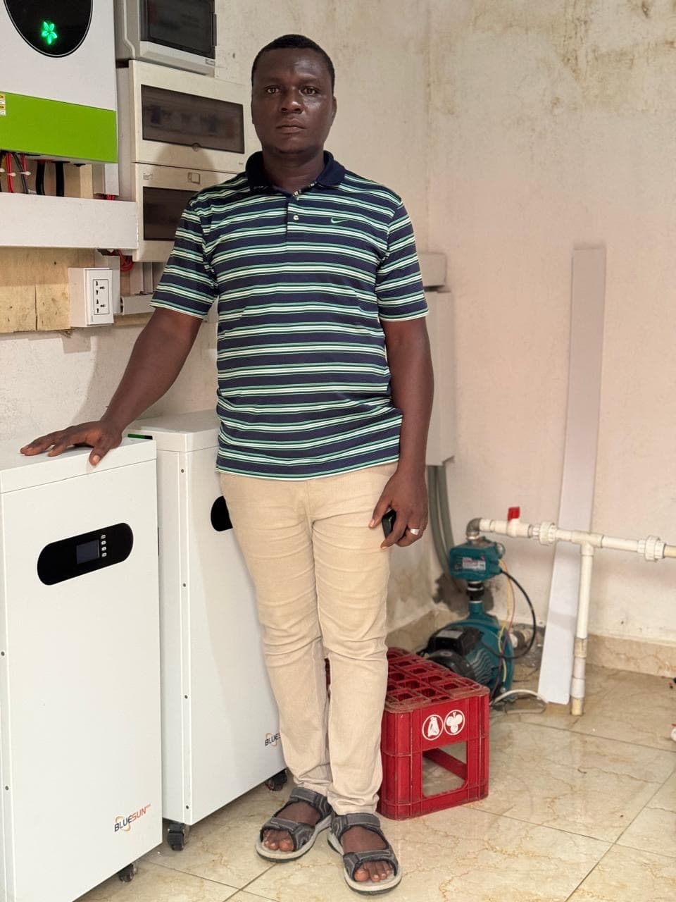 Technician standing beside a wall-mounted solar inverter and battery bank